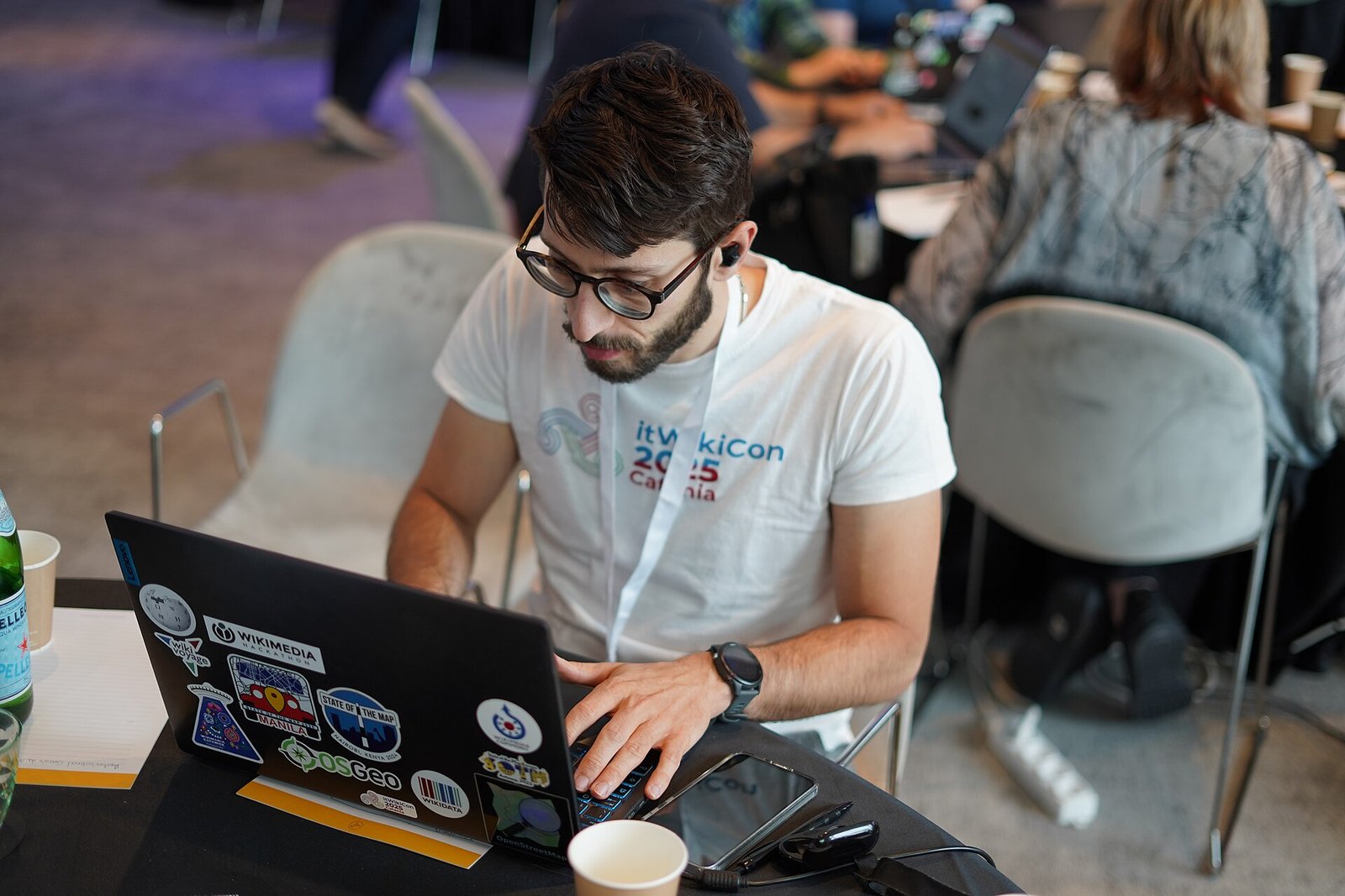 A software developer works on a laptop at the Wikimedia Hackathon in Milan, with colleagues nearby (file photo)
