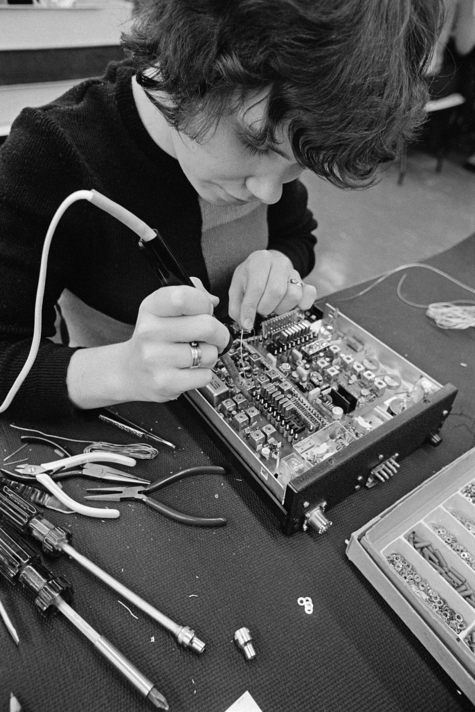 An electronics assembly worker solders a circuit board on a production line (archival illustrative photo)