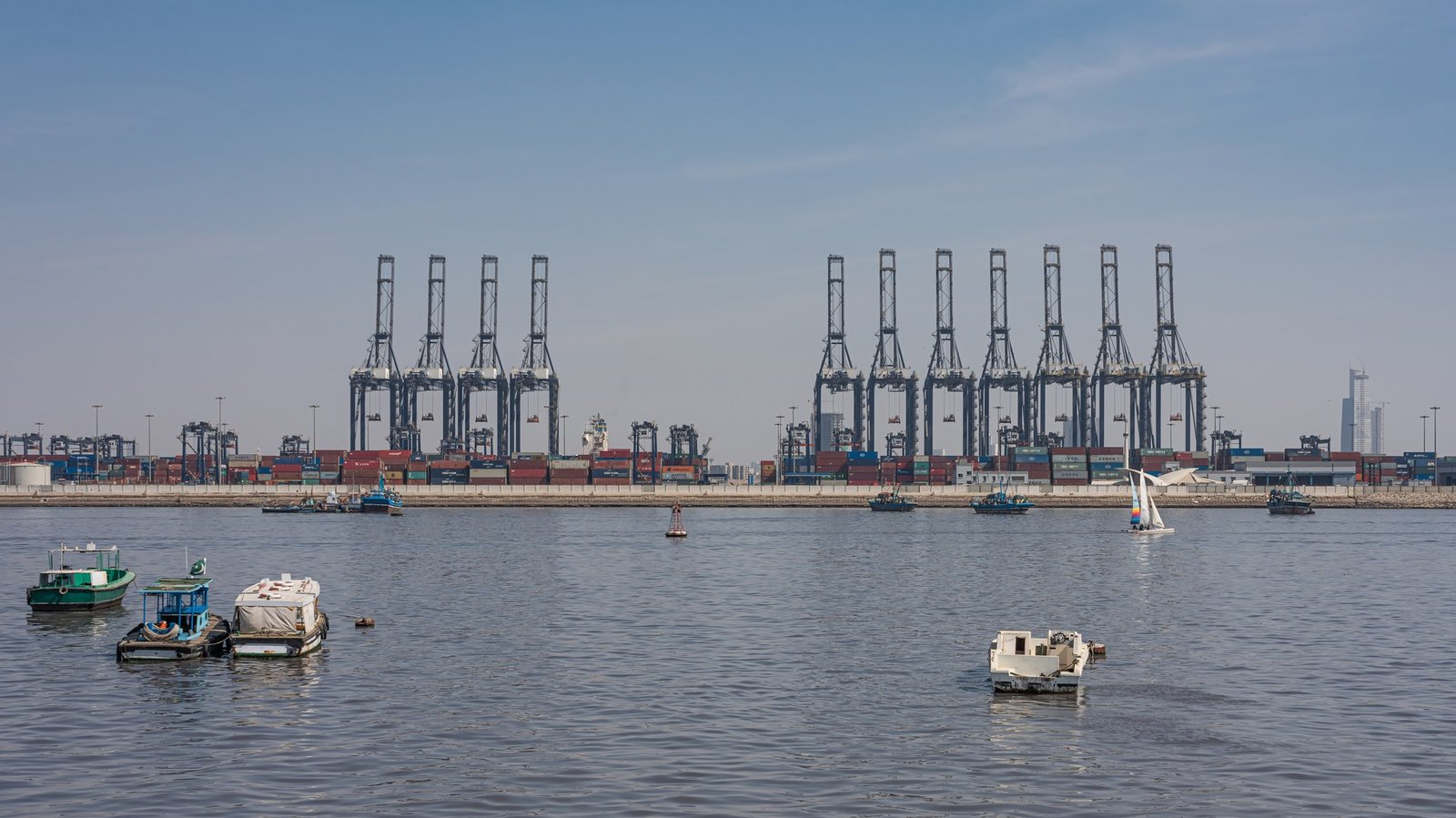 Container gantry cranes and stacked shipping containers at the port of Karachi, Pakistan, with small boats in the foreground.