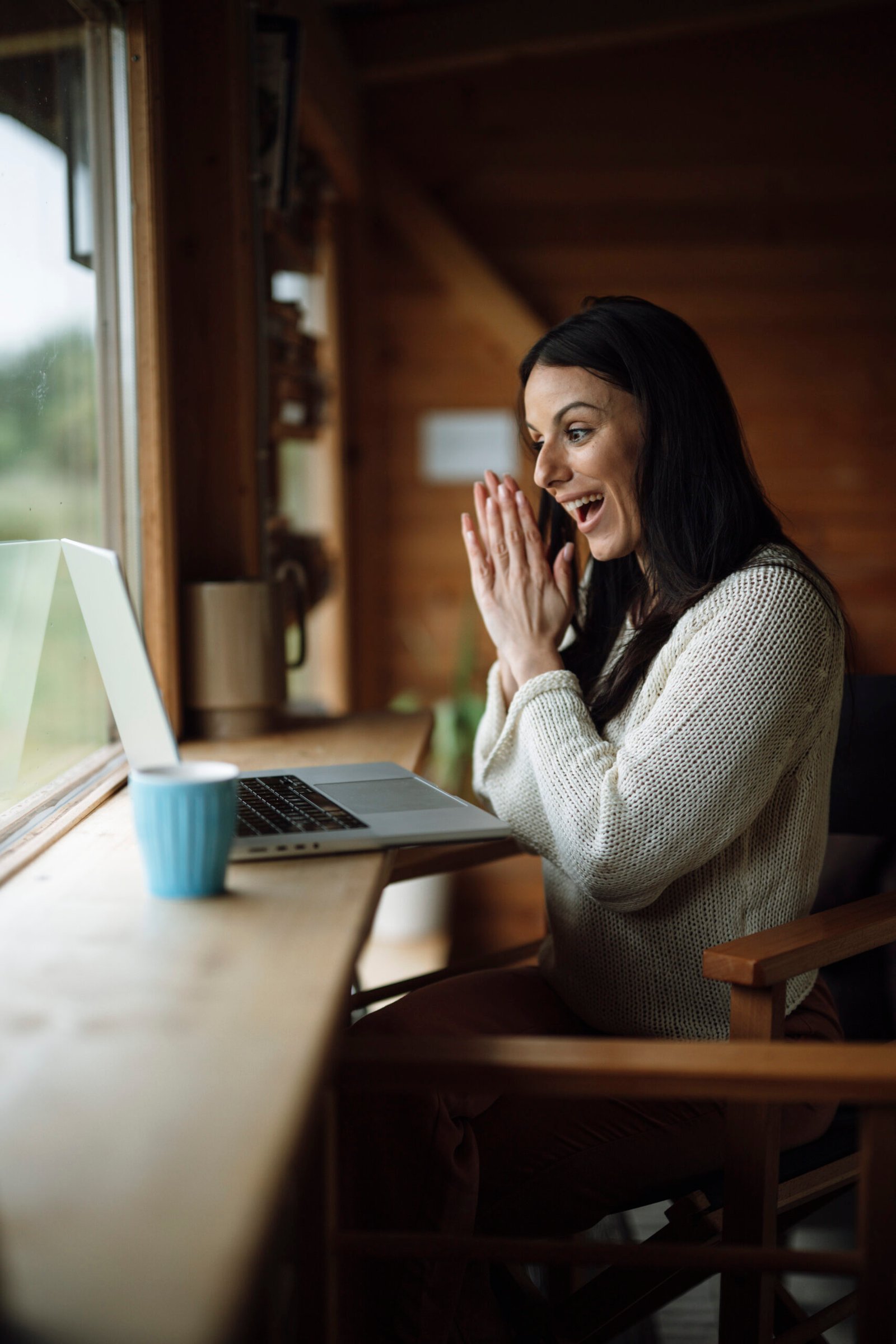 A woman on a video call using a laptop at a wooden table — representative photo.