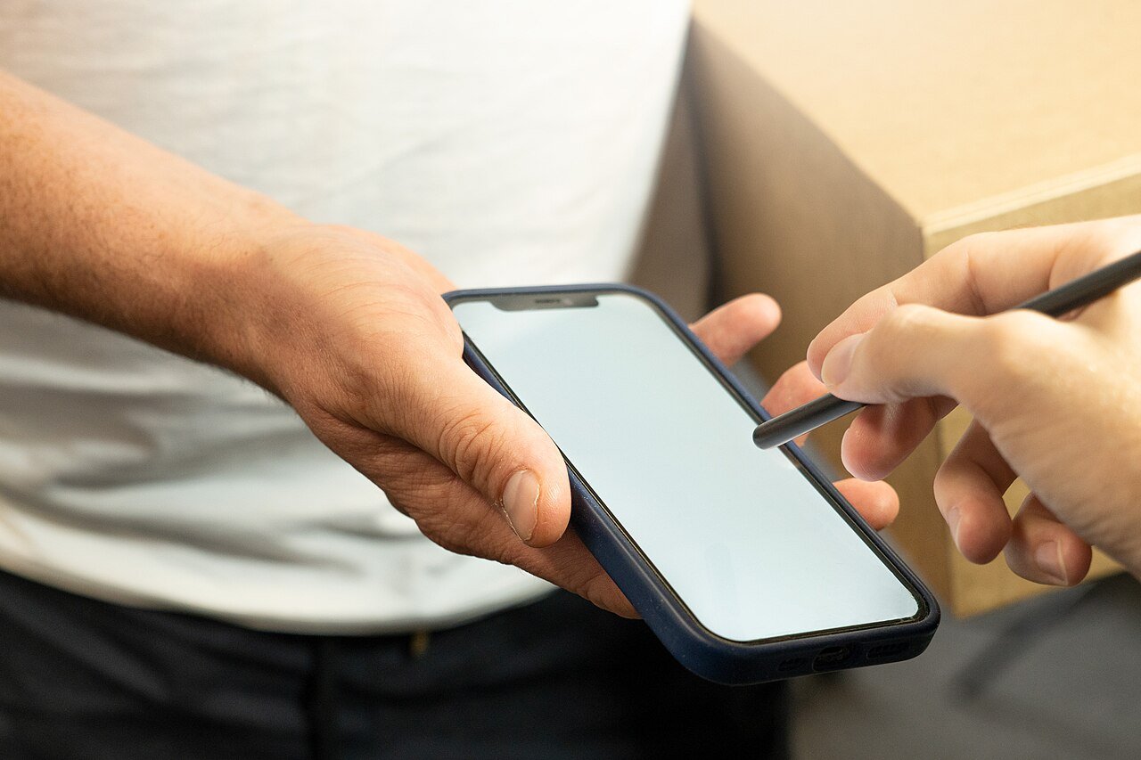 A hand verifying details on a phone — the PEC E-Card accessed through the NADRA Pak ID app can be presented for official verification. Photo: Meanwell Packaging, CC BY 2.0 via Wikimedia Commons