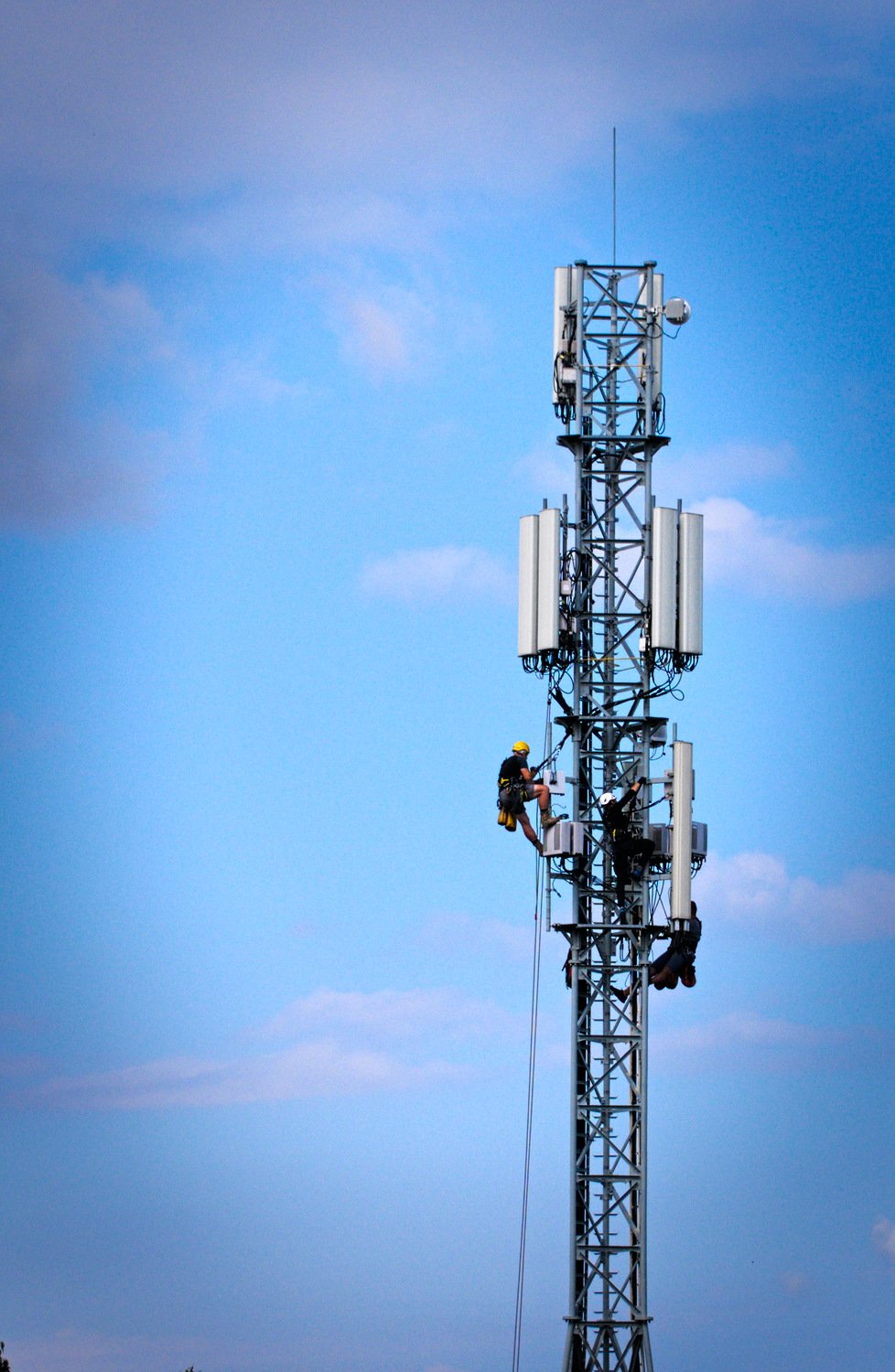 Technicians in safety harnesses climbing a cell tower — PTA wants at least 20% of 4G sites in the federal and provincial capitals upgraded to 5G